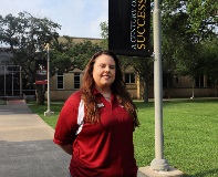 Bailey Koebrick in a maroon VC polo smiling outside with VC signage behind her