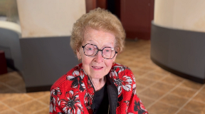 Dr Julia Riggs smiles wearing glasses and a red floral top