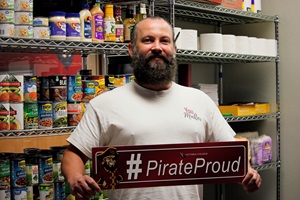 Thomas holds a #PirateProud sign inside of the Pirate Pantry with canned goods behind him