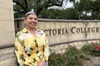 Tracy Edwards in a floral yellow dress beside a Victoria College sign