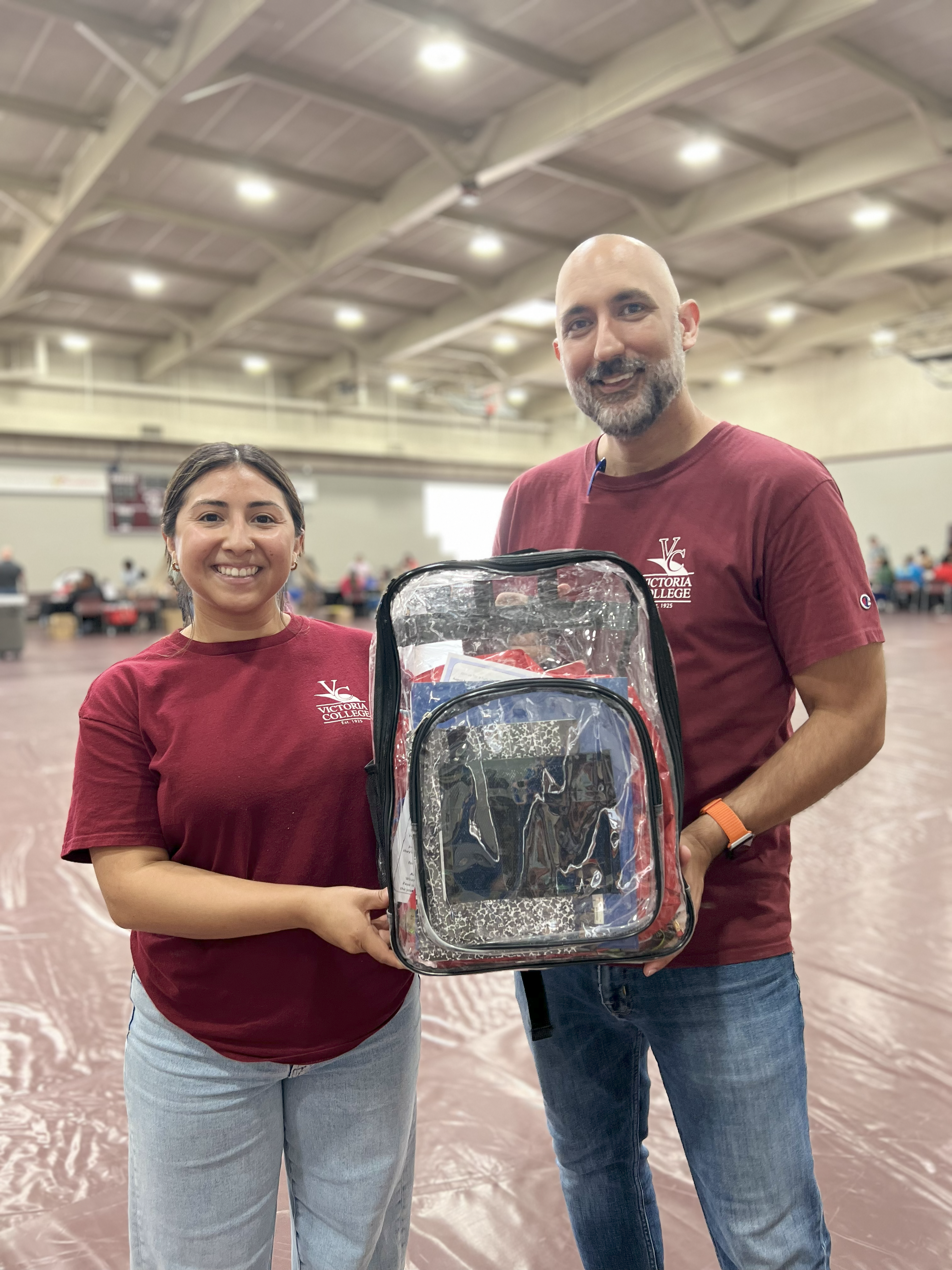 Two VC staff members smile and hold free back pack and school supplies